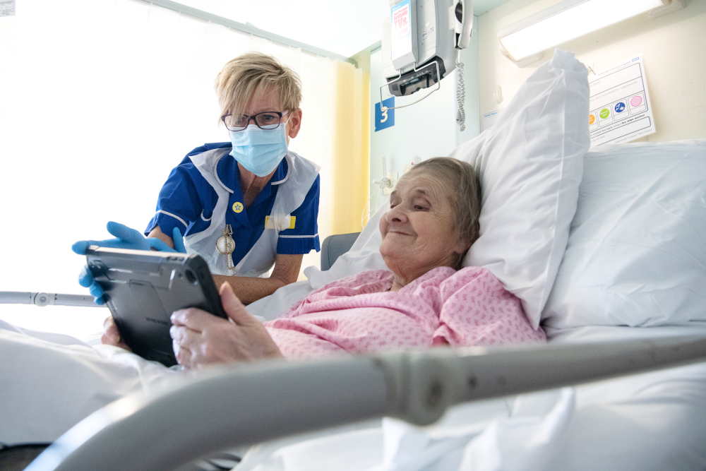 Elderly lady in hospital bed looking at iPad with nurse by her side